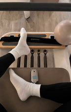 Feet in white socks on a Pilates reformer with the Sole Halo cooling mist resting alongside