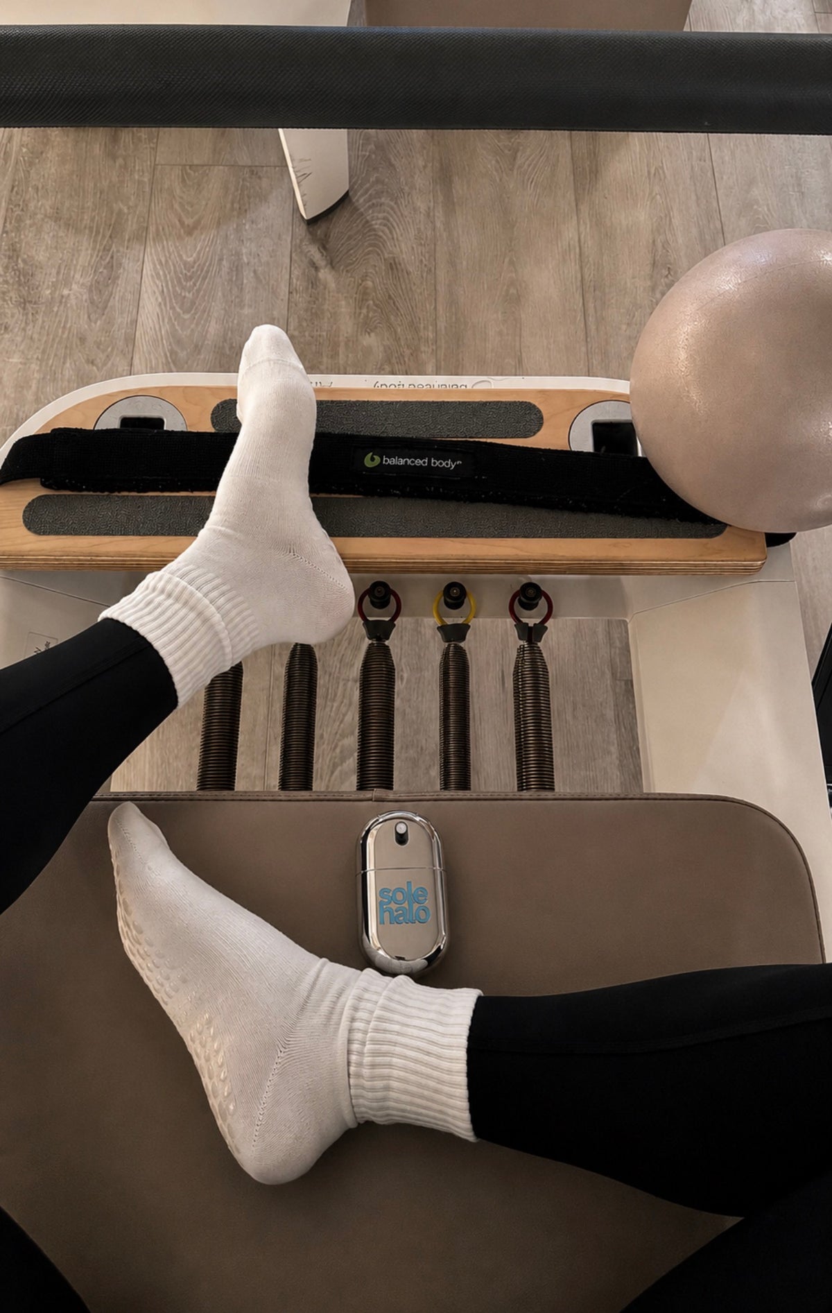 Feet in white socks on a Pilates reformer with the Sole Halo cooling mist resting alongside