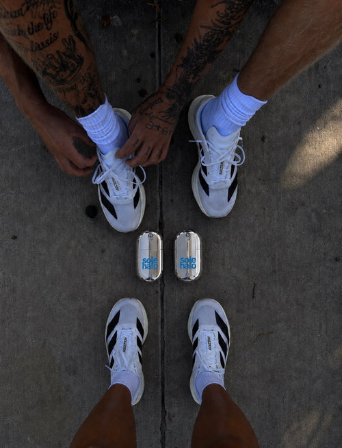 Two runners lacing up their shoes with a pair of Sole Halo cooling mist bottles between them